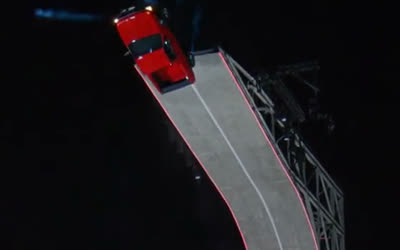 A car launching off the top of a giant curved ramp on blue jets at night